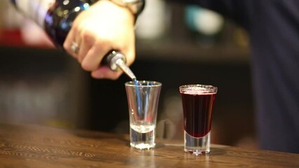 Bartender pours a blue drink in a glass and glass with red drink on the bar