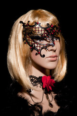 Mannequin with bright blond hair wearing a metallic half mask posing on a black background