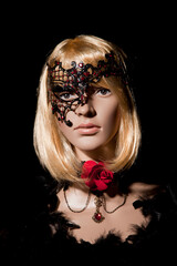 Mannequin with bright blond hair wearing a metallic half mask posing on a black background