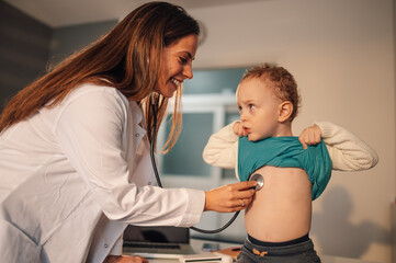 Female doctor or pediatrician examining boy patient in private clinic or at home