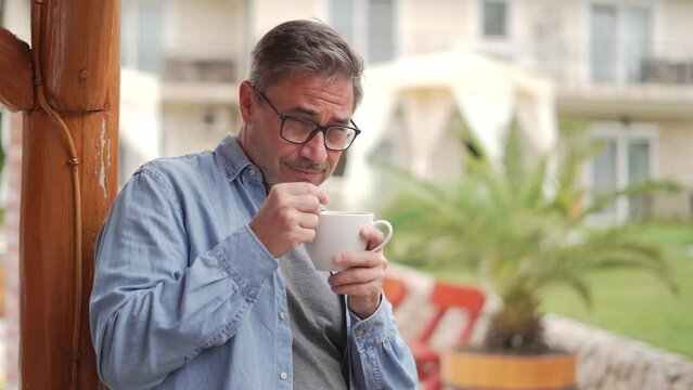 Portrait of happy middle aged man at home outdoor on terrace in garden, relaxing, drinking morning coffee, smiling.