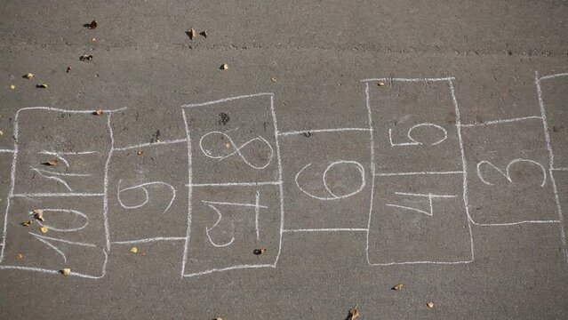 Girl playing hopscotch jumping on the numbers outside on a sunny day