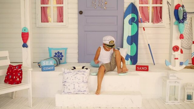 Boy sits on the doorstep and wears sandals in a room with sea decoration