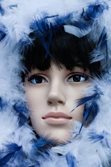 Plastic woman mannequin with black hair wearing a hoodie with white and blue feathers. Cool and shady natural light outside