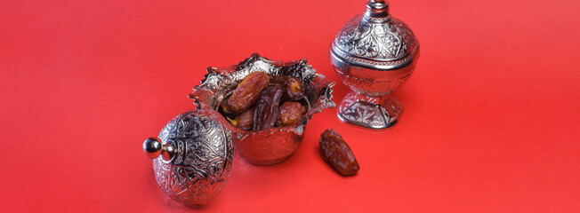 Dates in a silver bowl on a red background. An image of the month of Ramadan in Islam. The holy...