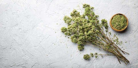 Dry wild oregano, Mediterranean aromatic herb in bunch and in wooden bowl on white plaster background, top view, space for text.