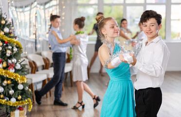 With unhurried music, teen boy and girl in couple spins to rhythm of tango during lesson for novice students in Christmas atmosphere. Classes in mini-groups for those who want to learn dancing
