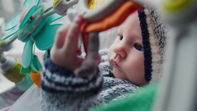 In a snug winter garment, an childs curiosity is piqued by the colorful overhead plaything. A blend of urban backdrop and homely warmth enveloping the scene.
