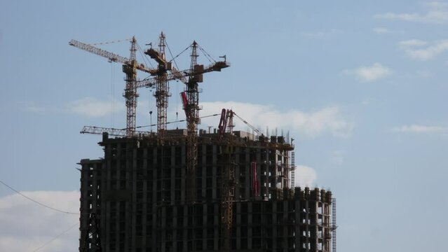 Four tall cranes work on construction site of residential house. Timelapse