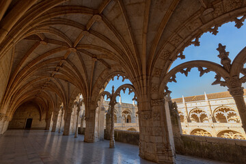Empty inner courtyard viewed through an ornate window at the historic Manueline style Mosteiro dos Jeronimos (Jeronimos Monastery) in Belem, Lisbon, Portugal, on a sunny day.