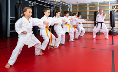 Fototapeta premium Karate kids in kimono performing kata moves with their teacher in gym during group training.