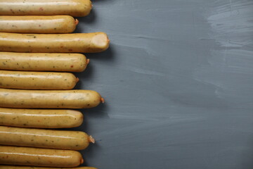 Chicken sausages with herbs lie next to each other on a gray background with space for copyspace text. Preparation for a barbecue picnic
