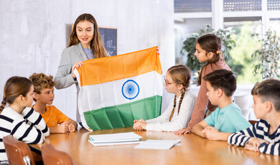 Group of preteen schoolchildren attentively watching pedagogue describing India flag in schoolroom