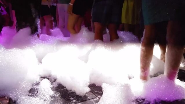 Legs of people dancing on deck of ship on foam party in stroboscope light