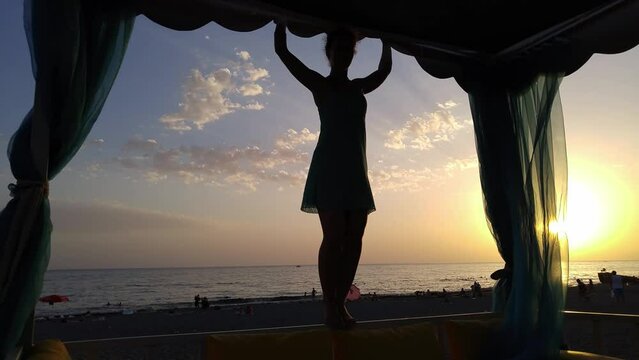 Silhouette of woman standing on border under tent in sunset on beach