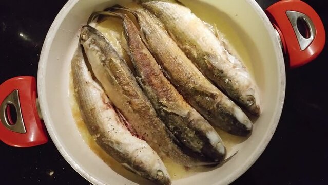 Five fried seabass fish in oil on frying pan close up, mobile phone video.