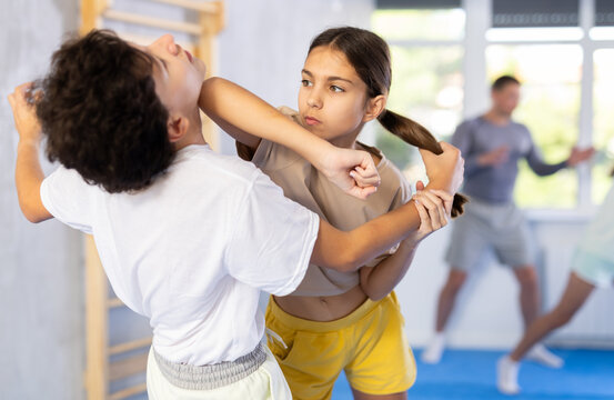 Boy and girl paired up and practice to aim stroke to neutralize opponent and repulse attack. Class self-defense training in presence of experienced instructor