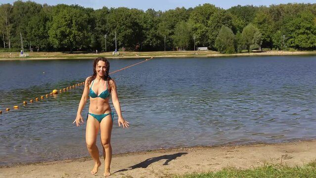 Wet woman in swimming suit go from water of pond at day