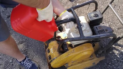 Hands of man holding red oilcan and refueling plate compactor close up