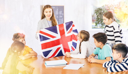 Positive female teacher discussing with preteens students state flag of Great Britain in auditory of middle school