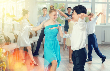 Couple of smiling teenagers, boy and girl in festive clothing performing graceful waltz with group...