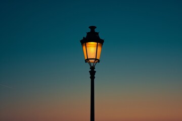 As the sky fades into a deep sunset, the outdoor street light illuminates the darkness with its warm, comforting glow, casting a sense of tranquility onto the quiet lamp-lit street