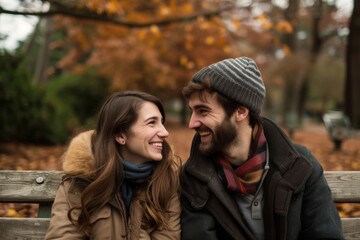 Fototapeta premium Amidst the vibrant autumn foliage, a couple shares a tender moment, their smiles radiating warmth as they embrace in cozy winter clothing