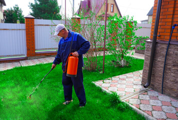 A man works in the garden, spraying weeds from a sprayer.