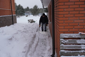 A man cleans snow in the winter in the courtyard of the house.