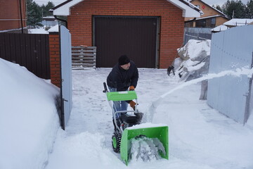 A man cleans snow in the winter in the courtyard of the house,  man cleaning snow with a snow blower