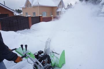 A man cleans snow in the winter in the courtyard of the house,  man cleaning snow with a snow blower