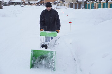 A man cleans snow in the winter in the courtyard of the house,  man cleaning snow with a snow blower