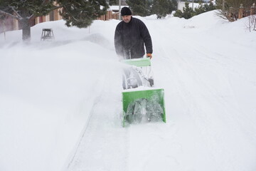 A man cleans snow in the winter in the courtyard of the house,  man cleaning snow with a snow blower