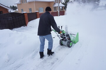 A man cleans snow in the winter in the courtyard of the house,  man cleaning snow with a snow blower