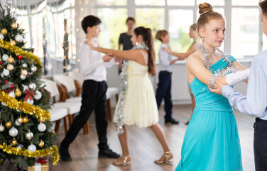 Positive teen boy and girl are dancing classic version of waltz in couple during lesson at studio in New Year atmosphere. Leisure activities and physical activity for positive children.