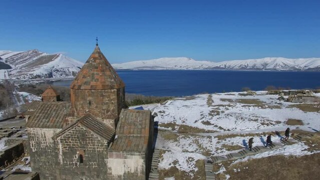 People walk near Sevan Monastery and Astvatsatsin Church