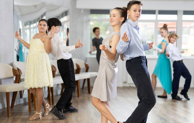 Fototapeta premium Group of positive teenagers, girls and boys, rehearsing jazz-style routine in dance studio. Partners standing back-to-back in pairs and snapping fingers..