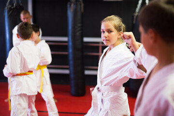 Diligent positive schoolchilds practicing new karate moves in pairs in class with trainer