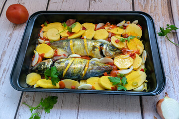 Tasty baked mackerel with potatoes and tomato, onion, lemon and spices in a baking dish.