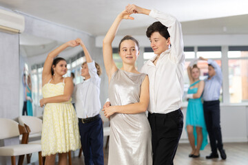 Positive teen boy and girl are dancing classic version of waltz in couple during lesson at studio....