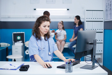 Caucasian female nurse using the computer desktop, to verify patient information and appointments,...