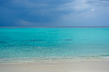 Fototapeta na wymiar Purplish sky and rain in distance at Caribbean sea, beautiful turquoise water under dark blue clouds.