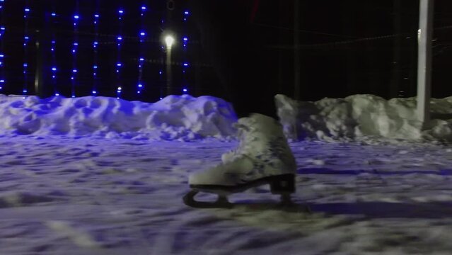 Woman in white skates slides by snowy ice at winter night. 