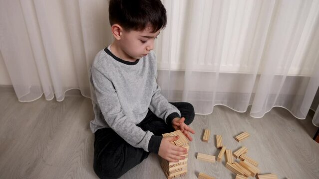 cute preschool boy playing with eco wooden toy pieces sitting on floor.kid building one piece over another, rectangles shapes. Stackable tumbling blocks game.4k