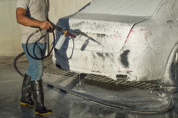 An adult man cleaning and washing a car with a foam gun.