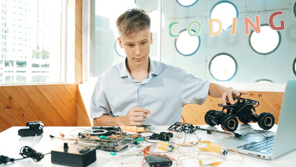 Highschool boy fixing car model with laptop and electric tool placed on table. Closeup of teenager...
