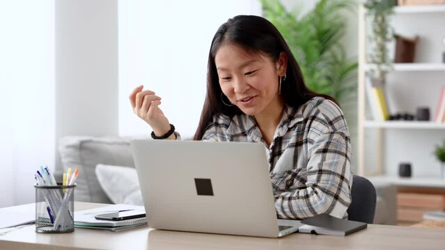 Chinese young woman having video call on laptop. Person talking online in the living room.