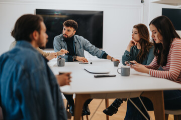 Focused group of professionals engaged in a serious discussion at a well-lit office meeting room with digital devices present.