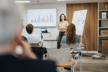 Focused business team engaging with a success-driven female presenter showing bar graphs and statistics on a screen in a modern conference room. - obrazy, fototapety, plakaty