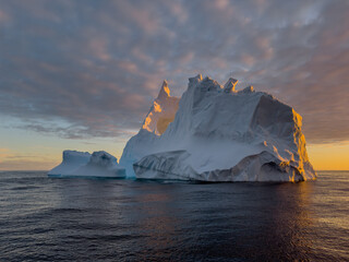 A huge high breakaway glacier drifts in the southern ocean off the coast of Antarctica at sunset, the Antarctic Peninsula, the Southern Arctic Circle, azure water, cloudy weather